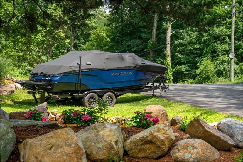 Covered blue MasterCraft boat on a trailer beside a driveway.